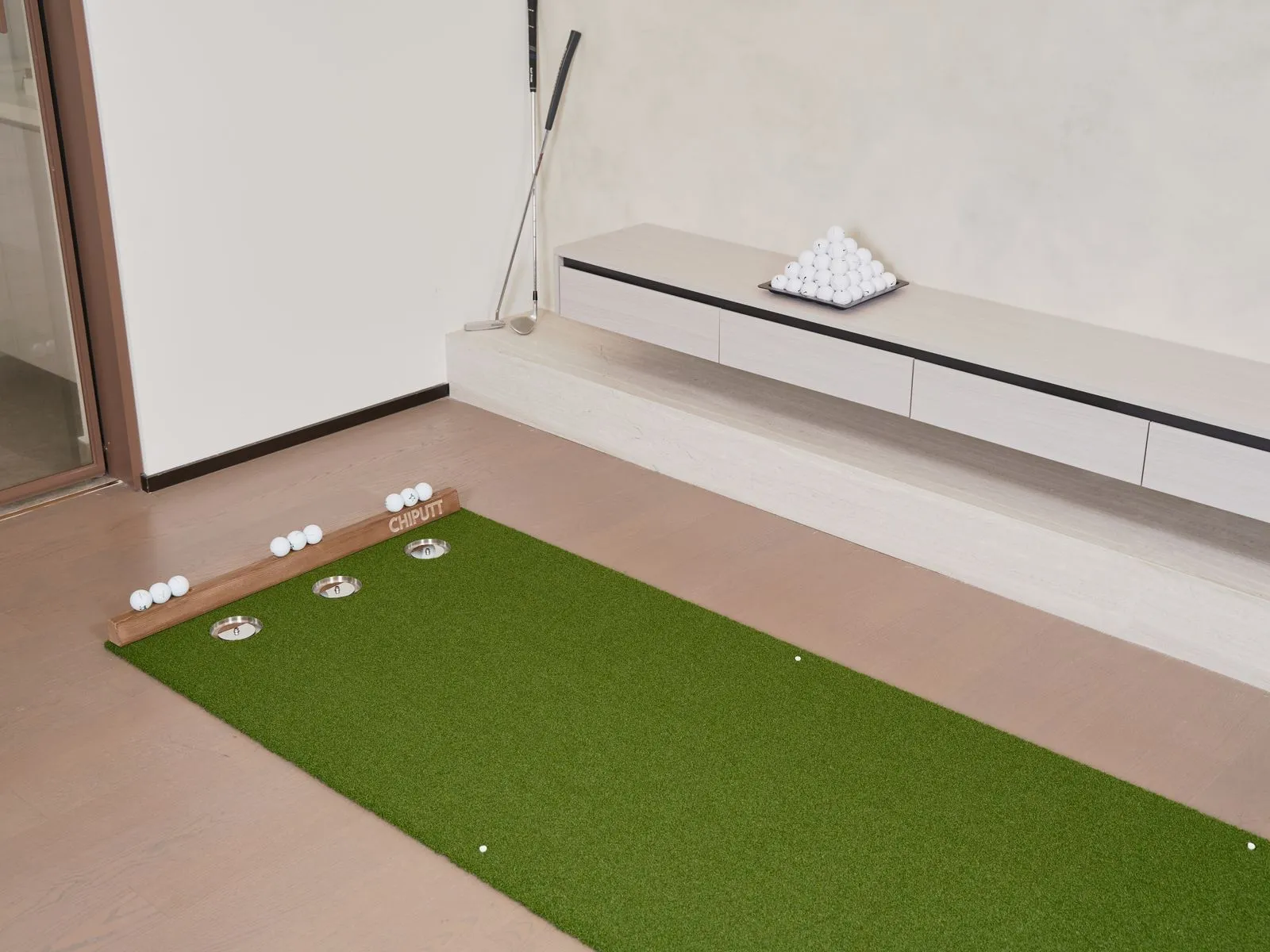 Indoor setup for golf practice with a putting mat, golf balls, and equipment.